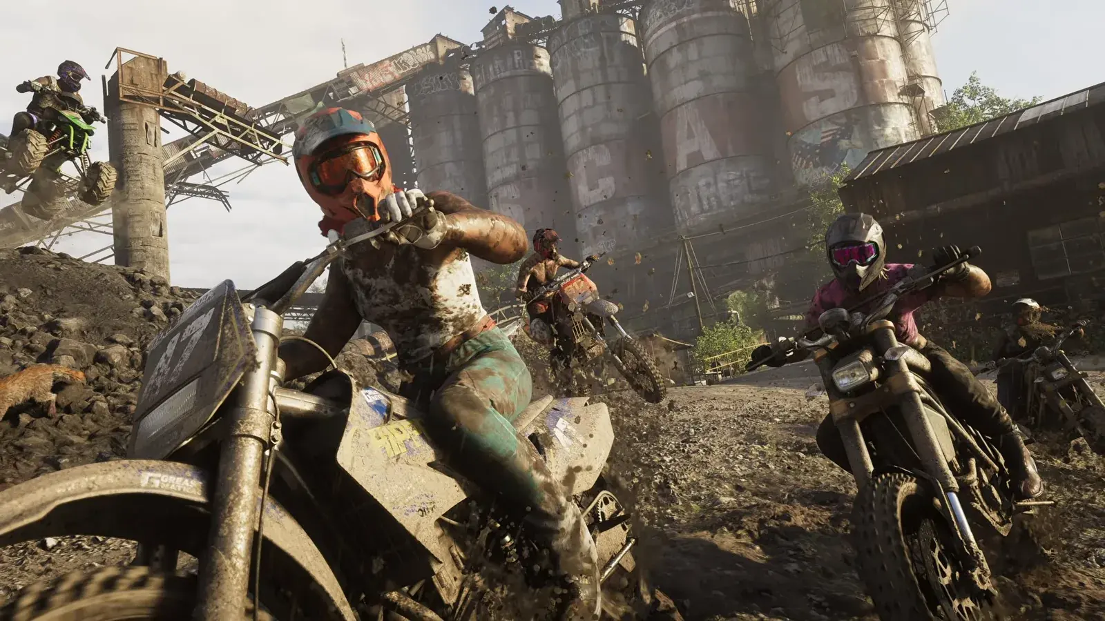 Dirt bike riders in mud in front of an abandoned industrial plant