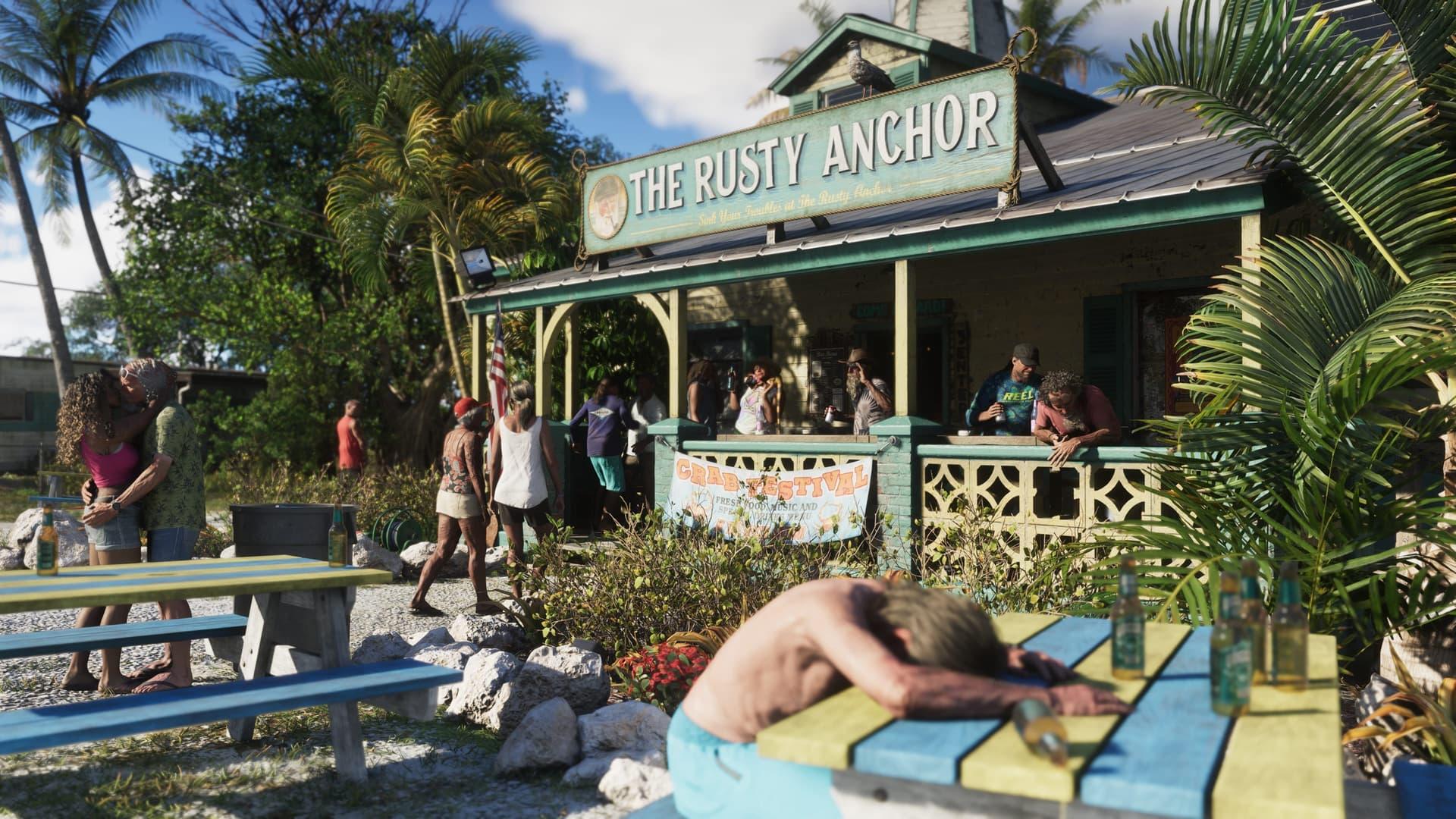 A busy wooden beach bar with a porch crowd and a man lying on a picnic table