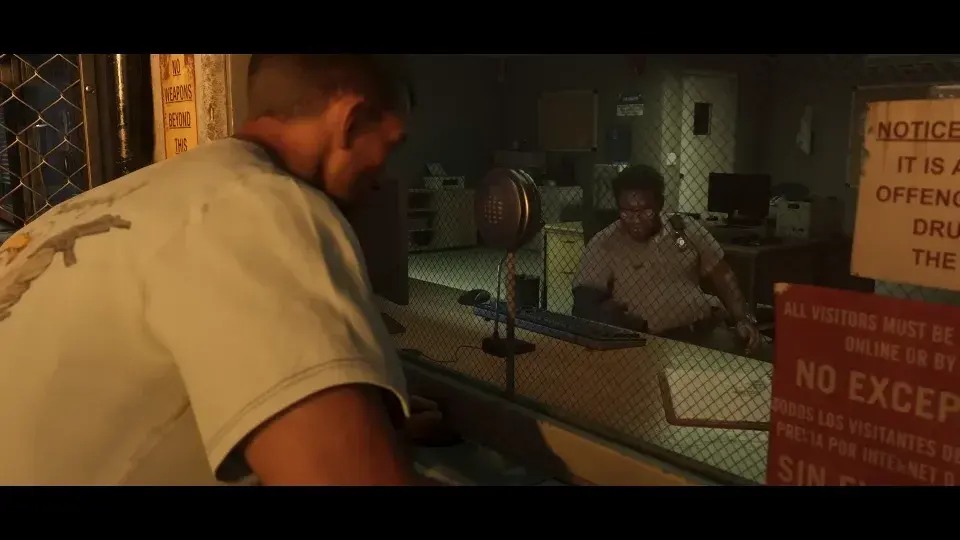 Jason mit kurzen Haaren in einem hellen T-Shirt beugt sich über den Besuchertresen eines Gefängnisses, hinter Glas ein Wärter und an der Wand Warnschilder