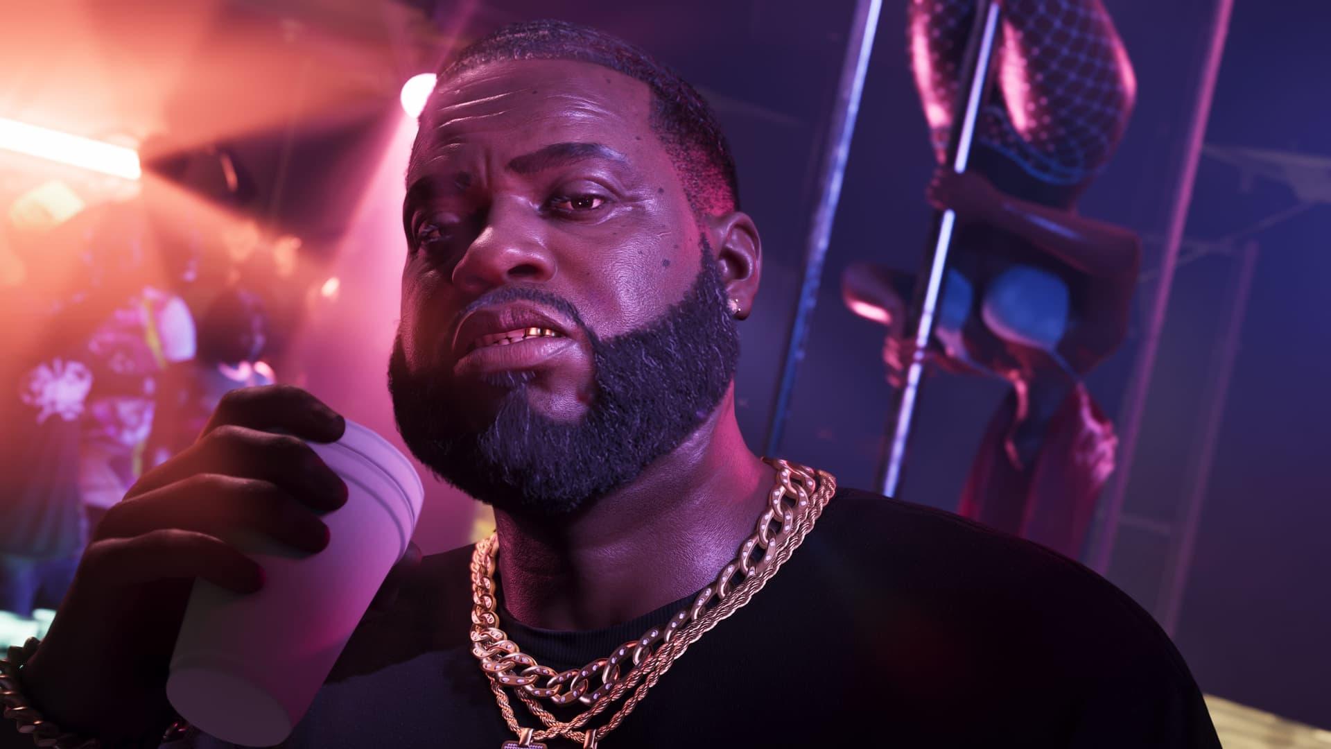 Nahaufnahme von Boobie Ike in dicken Goldketten mit einem Becher in der Hand, in einem rosa beleuchteten Club, hinter ihm eine Tänzerin an der Stange, in einem offiziellen GTA-6-Screenshot