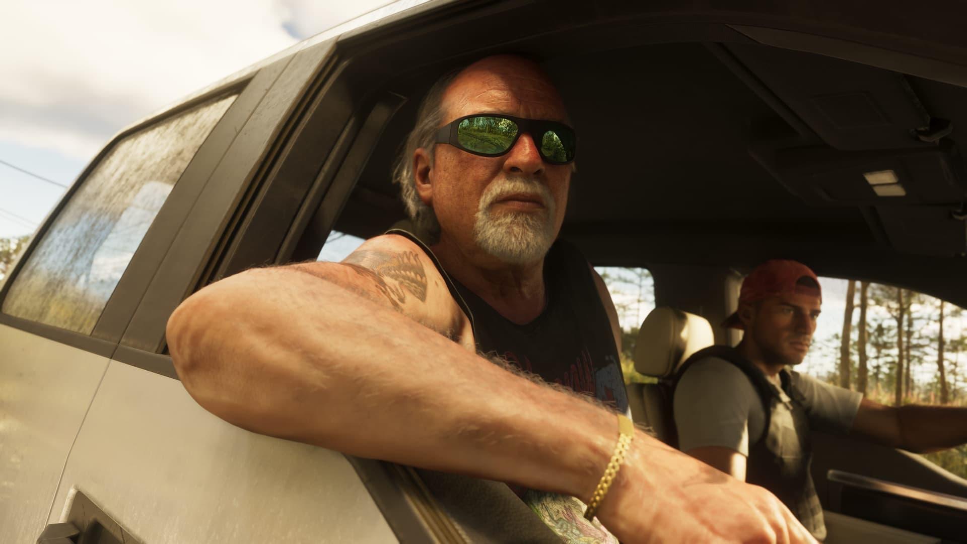 Brian Heder, ein Mann mit weißem Bart und grün verspiegelter Sonnenbrille, lehnt sich aus einem Lkw-Fenster, während ein Mann mit roter Kappe fährt, in einem offiziellen GTA-6-Screenshot