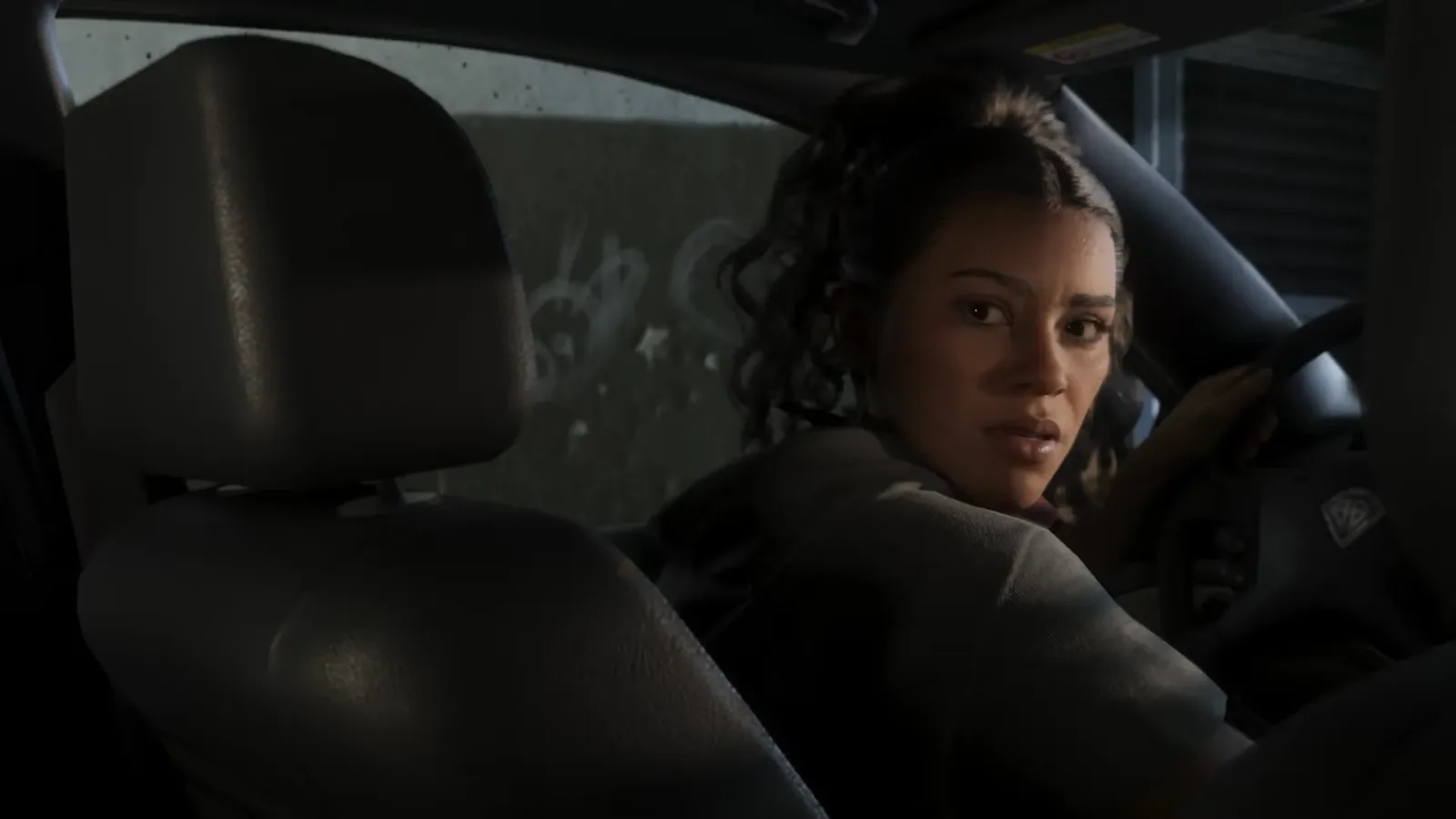 Lucia at the wheel of a dark car looking back over her shoulder in Rockstar footage of GTA 6, steering wheel in her hand
