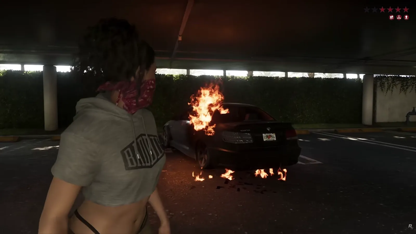 Lucia in a bandana mask watching a black sedan burn in a GTA 6 parking garage with four red wanted stars and three icons on the HUD