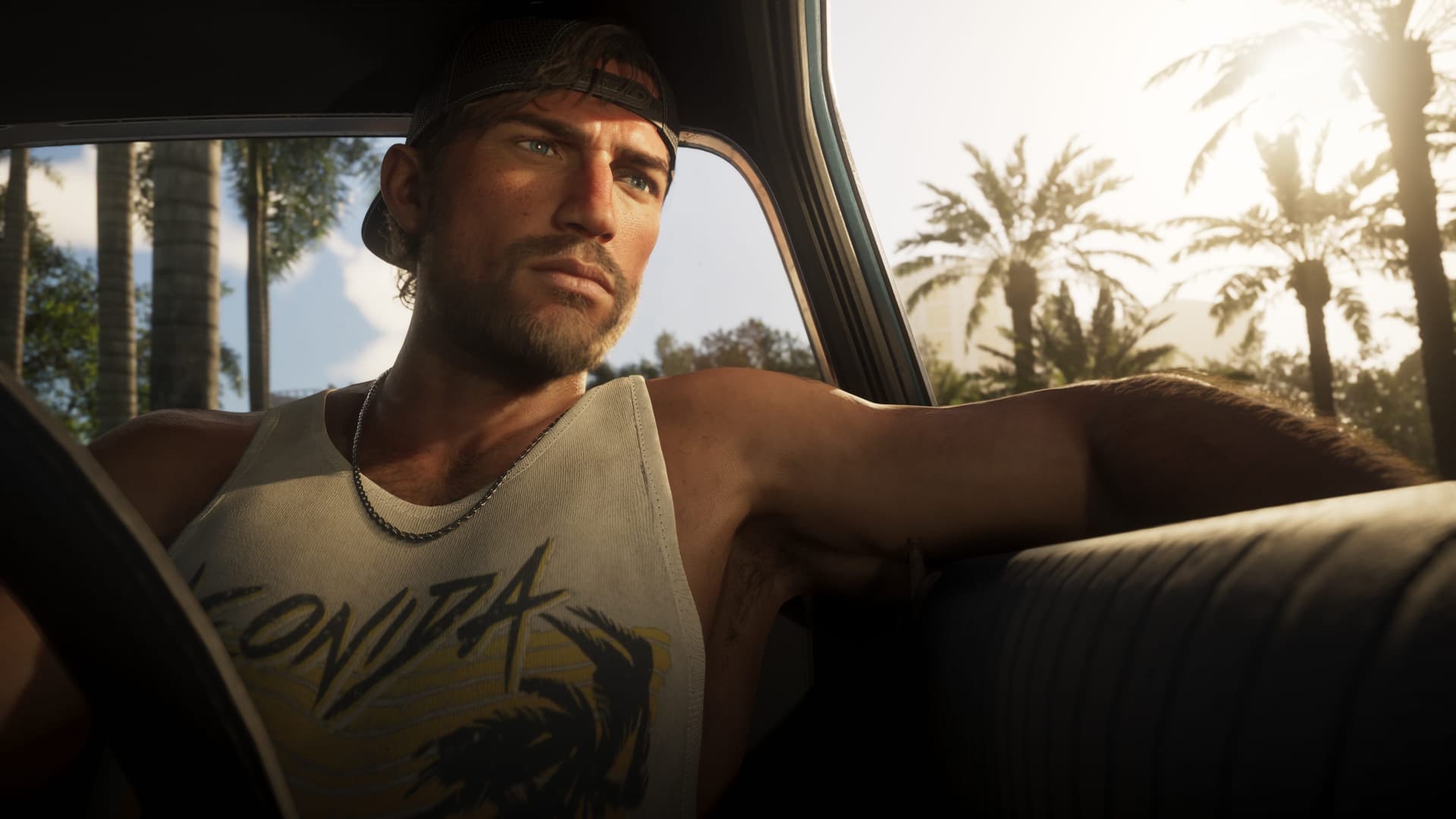 Jason Duval in a car seat wearing a backwards cap and a tank top with palm trees behind him in an official GTA 6 screenshot